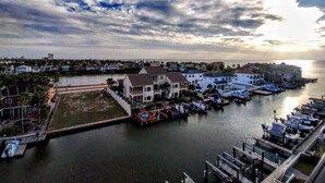 A marina with docked boats, a waterfront property with multiple buildings, and a view of the sea under a cloudy sky.