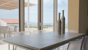 Et moderne spiseområde med et stort bord og stole, store vinduer med udsigt over landskabet, og to dekorative vaser på bordet.