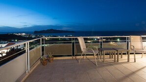 En balkon med stole og plantekasser, med udsigt over bybilledet om natten.