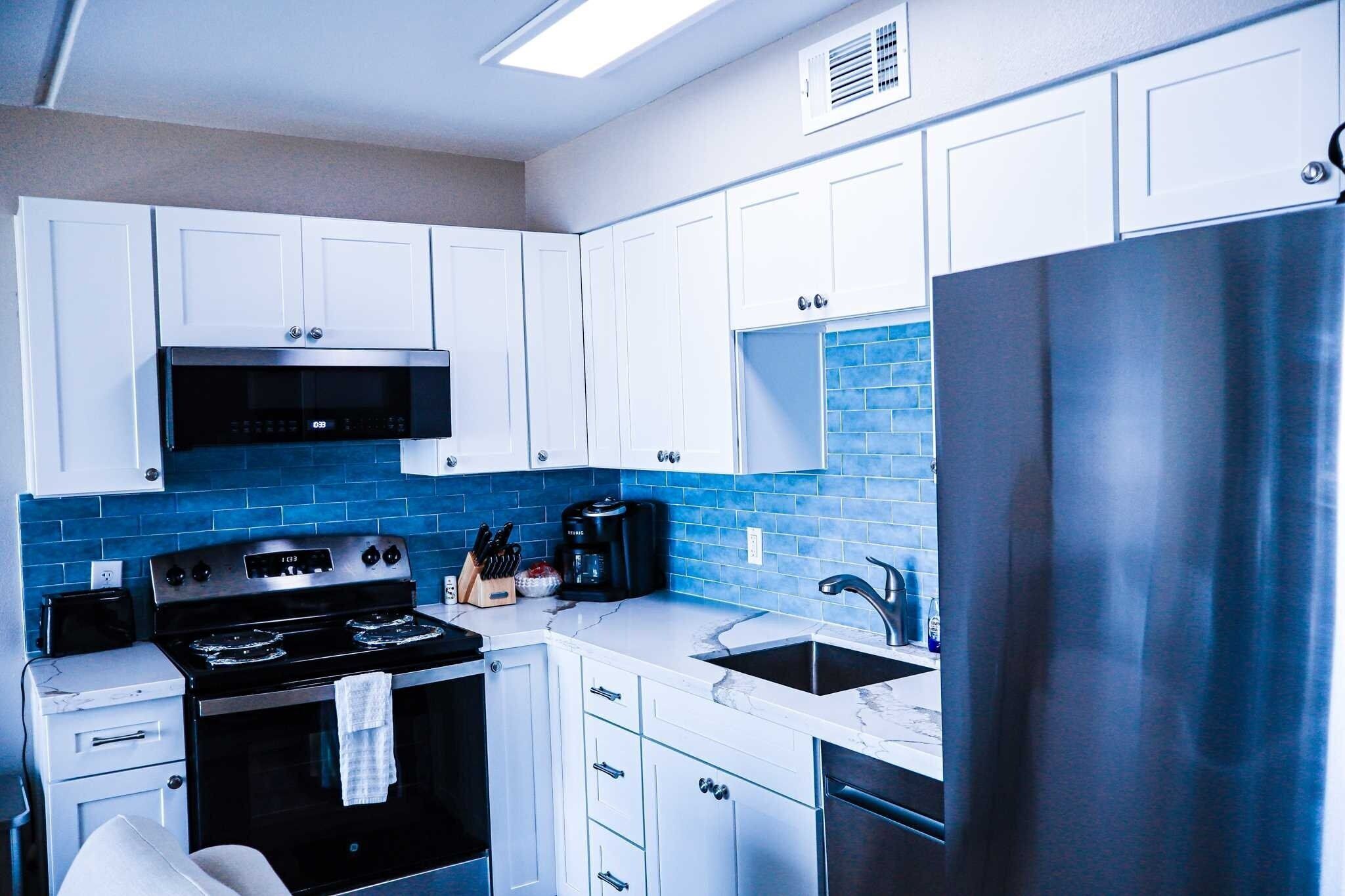 A modern kitchen with white cabinets, a stainless steel refrigerator, a black stove, and a blue-tiled backsplash.