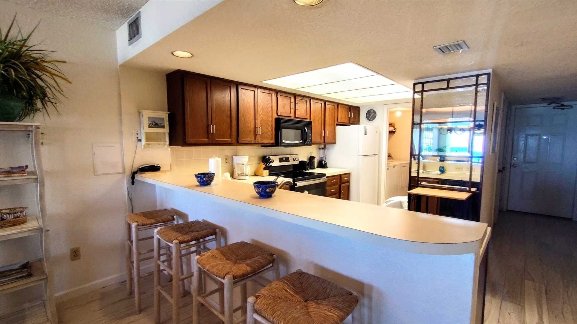 Une cuisine avec des meubles en bois, un four à micro-ondes, un réfrigérateur et un coin bar avec des tabourets.