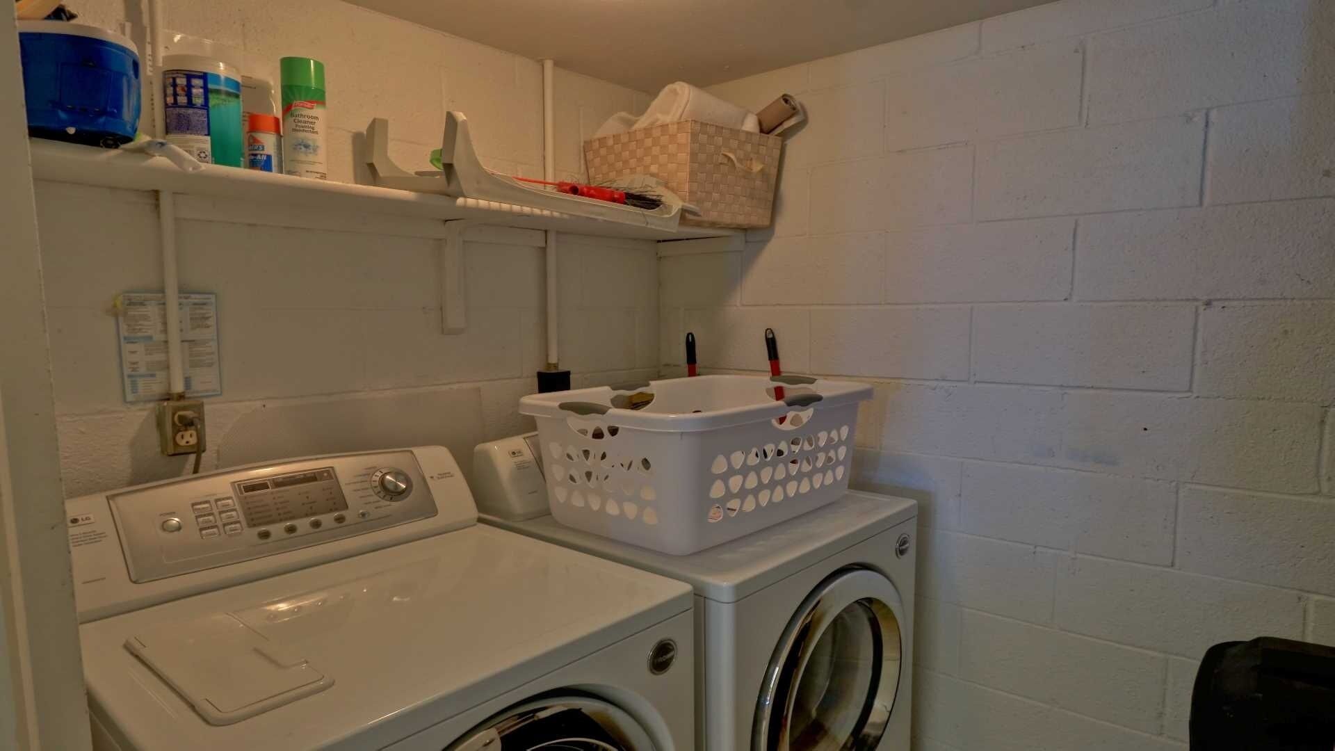 Een wasruimte met een wasmachine en droger, een plank met schoonmaakmiddelen en een wasmand.