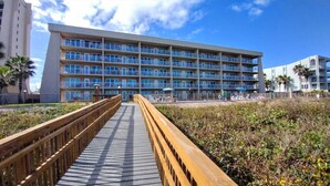 A multi-story hotel with balconies, a wooden boardwalk leading to the entrance, and a clear blue sky. - Edgewater 507 Minium 3 Bedroom Condo by RedAwning (South Padre Island)