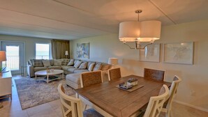 A spacious living area with a large sofa, a dining table, and a balcony with a view. - Edgewater 507 Minium 3 Bedroom Condo by RedAwning (South Padre Island)