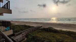 Vista a la playa desde un balcón, con un paseo de madera que lleva a la orilla.