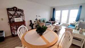Una sala acogedora con una mesa redonda de madera, sillas blancas, un sofá y un televisor.