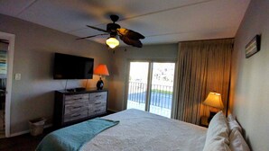 Ein Hotelzimmer mit Bett, Deckenventilator, Fernseher, Kommode und einem Balkon mit Vorhängen.
