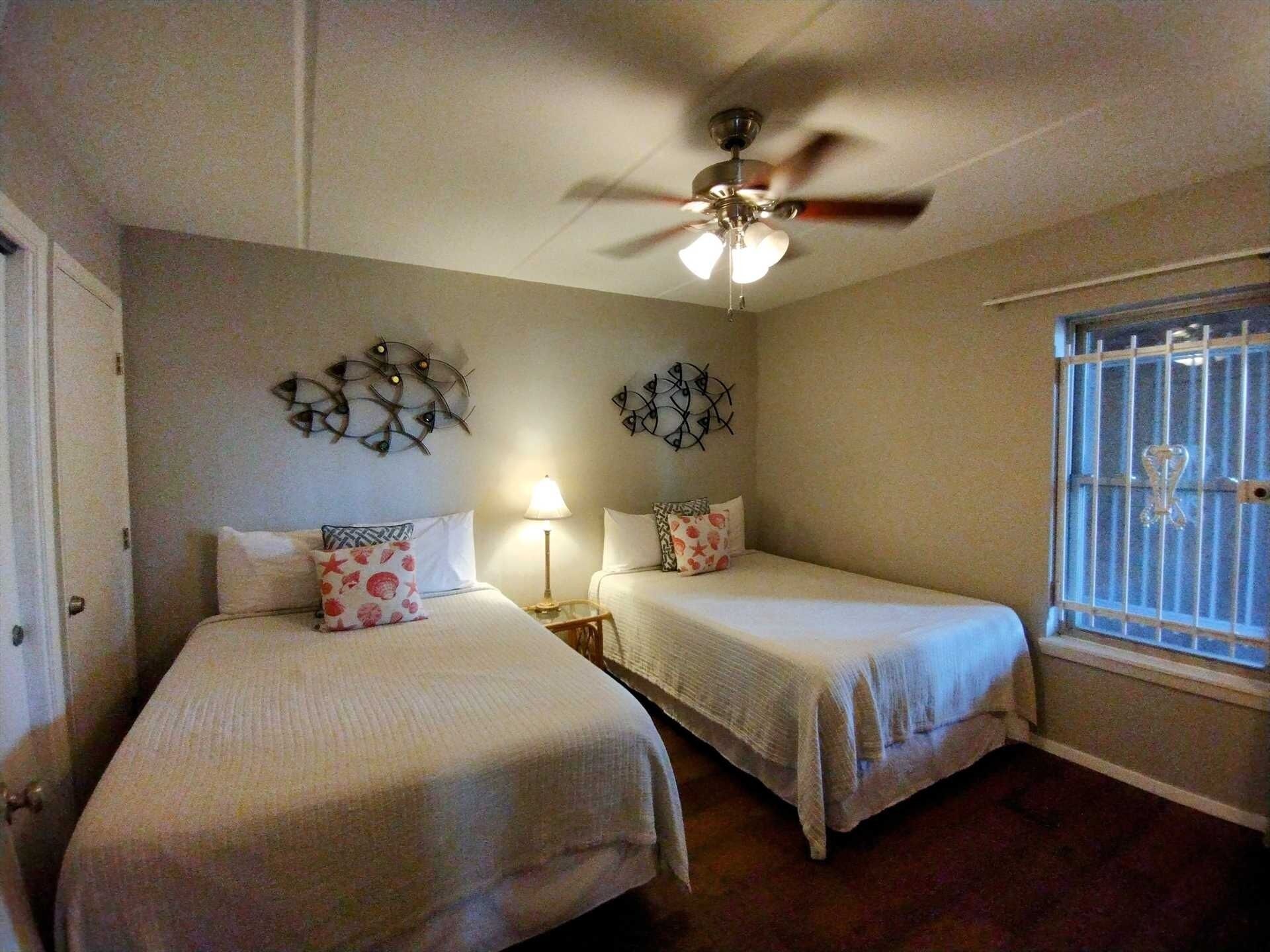 A bedroom with two beds, a ceiling fan, decorative wall art, a window with bars, and a door.