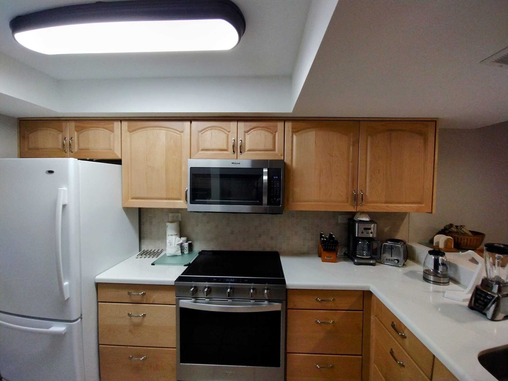 Una cocina moderna con armarios de madera, un refrigerador de acero inoxidable, un microondas, una estufa y una cafetera.