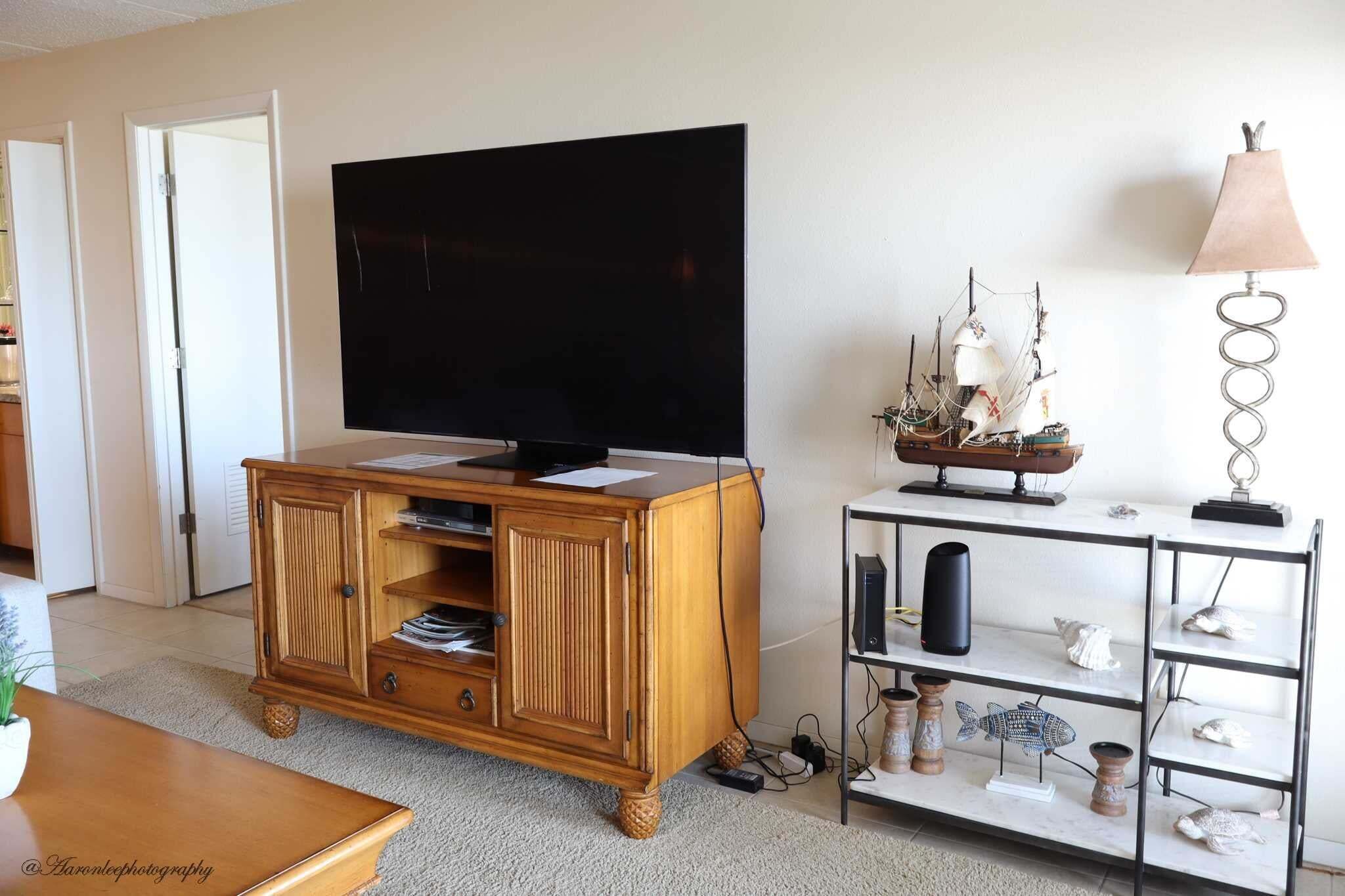 A living room with a wooden entertainment center, a flat-screen TV, and a decorative shelf with seashells and ship models.