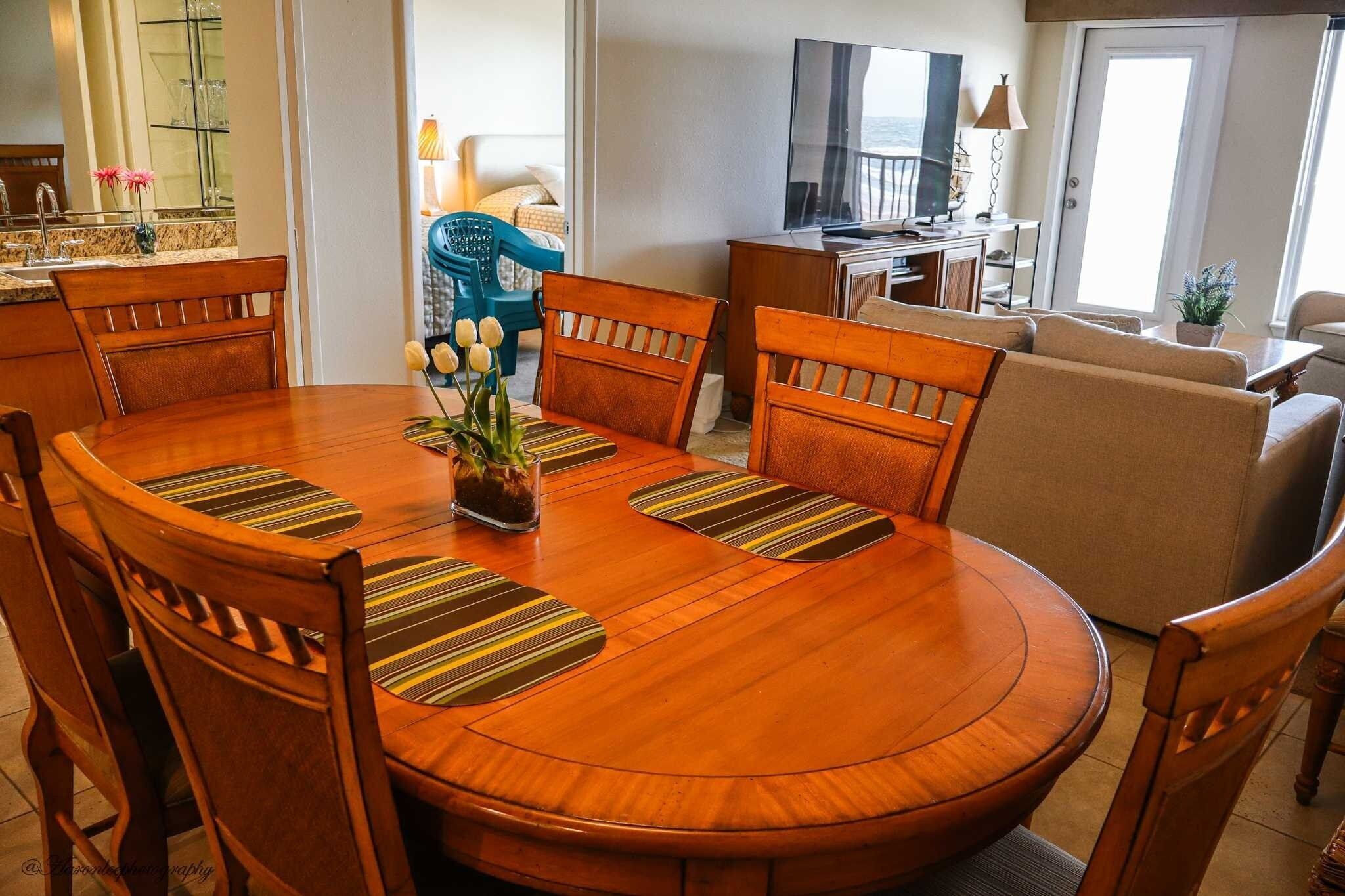 Un coin repas avec une table ronde en bois, six chaises et un vase rempli de fleurs.