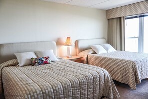 Une chambre d’hôtel avec deux lits, chacun recouvert d’une courtepointe à carreaux, une lampe de chevet et une fenêtre avec des rideaux.