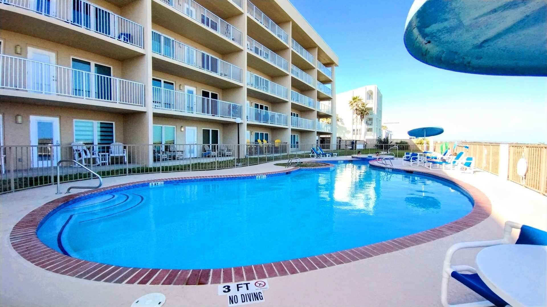 A hotel with a pool surrounded by lounge chairs and a sign indicating a 3 ft depth limit.