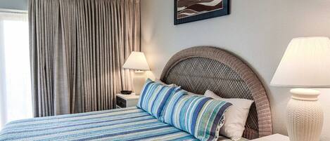 Habitación de hotel con cama, dos lámparas de noche, un ventanal con cortinas y un cuadro en la pared.