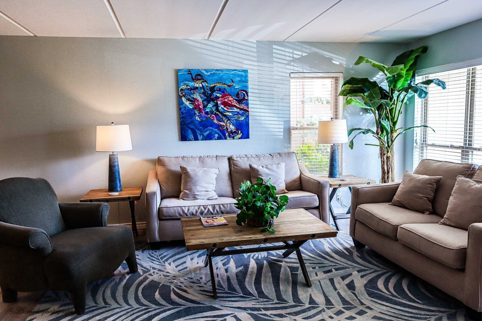 Un salon avec un canapé, un fauteuil, une table basse et un tableau accroché au mur.