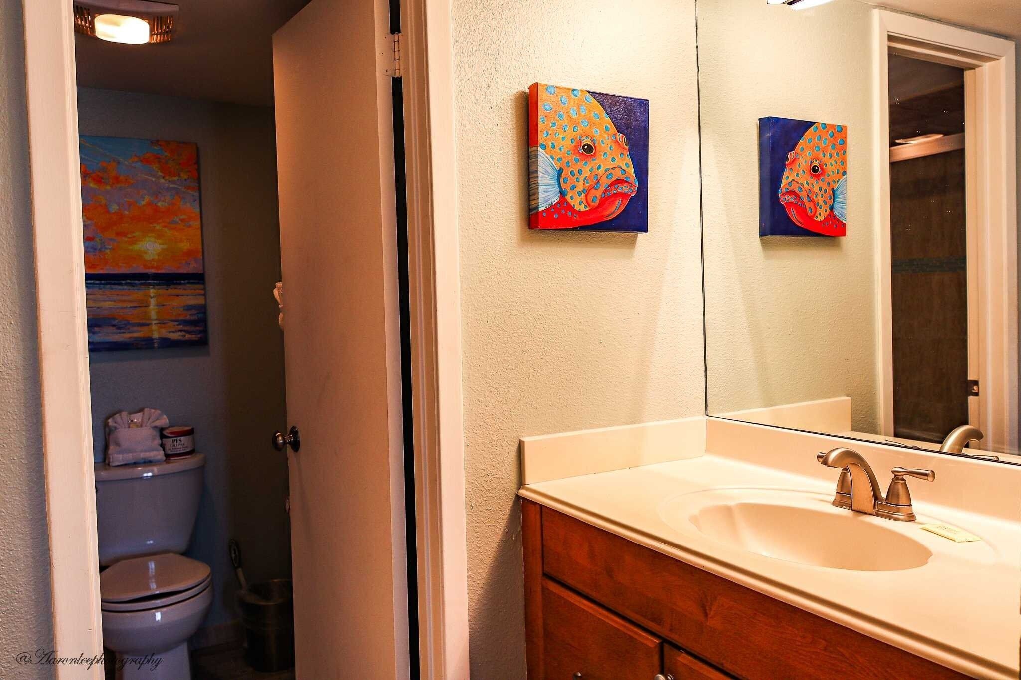 Uma casa de banho com uma pia branca, um espelho e duas pinturas na parede.