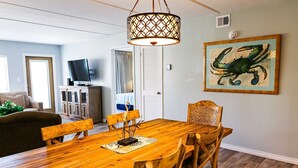 Un coin repas avec une table et des chaises en bois, un luminaire suspendu et une œuvre d’art encadrée au mur.