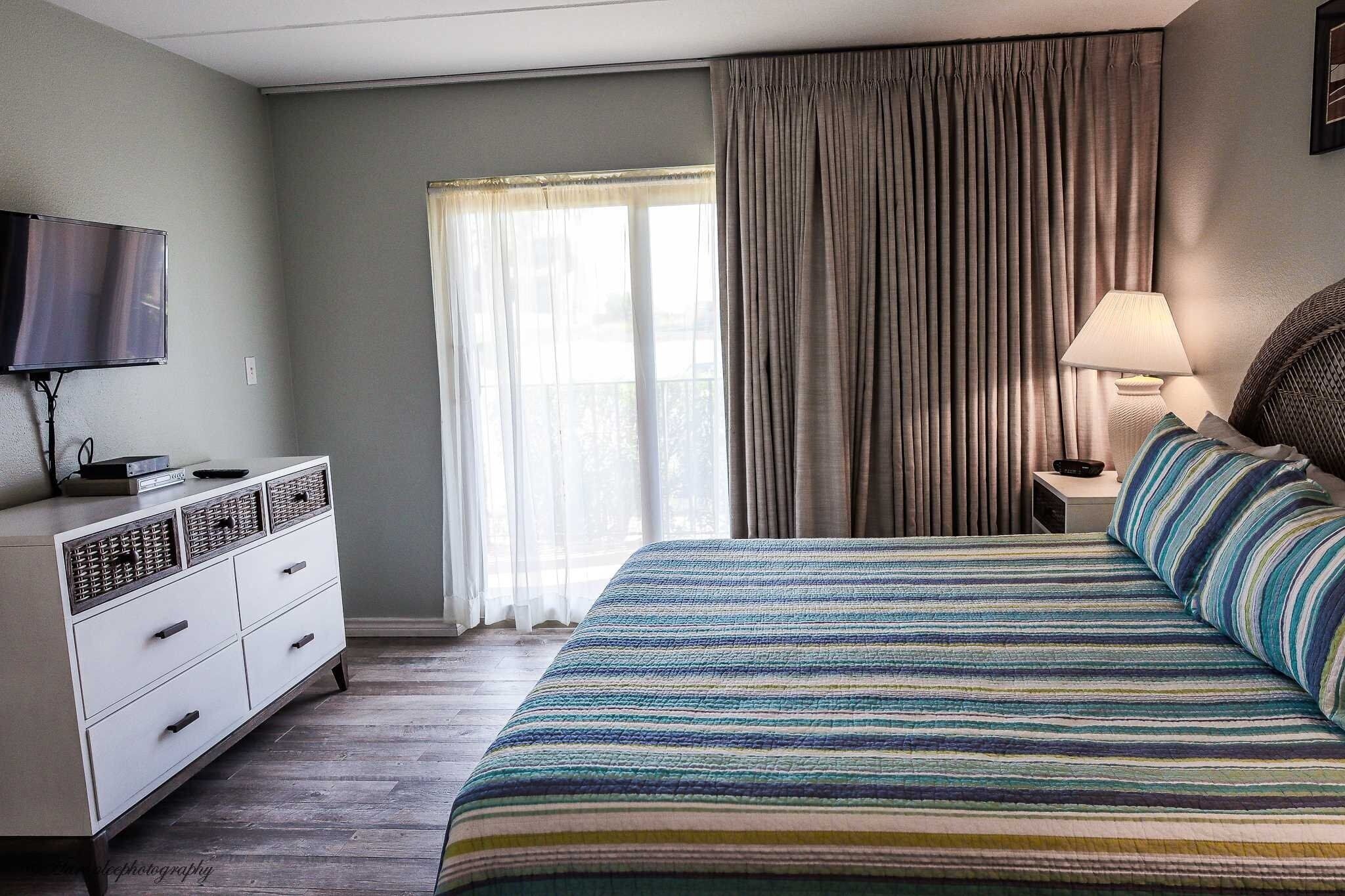 Une chambre d’hôtel avec un lit, une télévision, un bureau et une fenêtre avec des rideaux.
