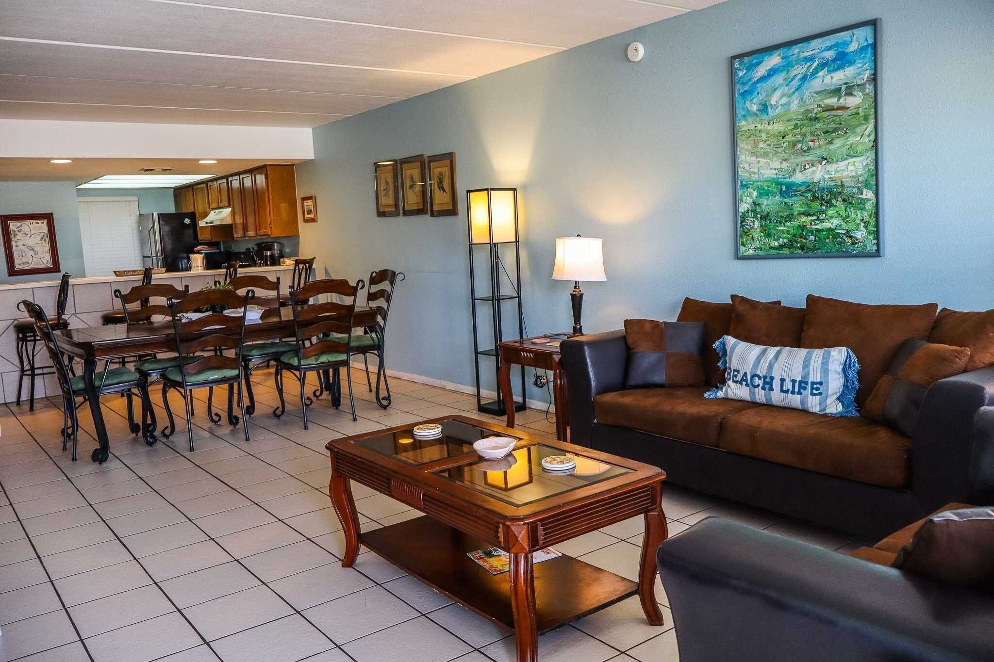 A living room with a brown sofa, a wooden coffee table, and a dining area with chairs and a table.