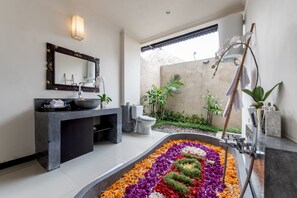 A modern bathroom with a large mirror, a sink, a toilet, and a decorative flower arrangement in the floor. - Villa Cendrawasih (Taro)