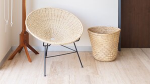 Une pièce comprenant un porte-manteau en bois, une chaise en osier et un panier tressé. Deux tableaux encadrés sont accrochés au mur.