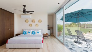 Une chambre moderne avec un grand lit, un ventilateur de plafond et une vue sur une terrasse extérieure aménagée avec des chaises et une table.