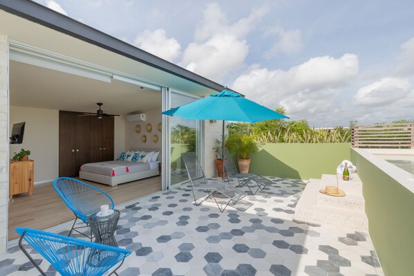 An outdoor patio with hexagonal tiles, a blue umbrella, and a bed visible through a glass door.