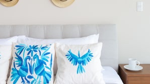 Une chambre à coucher bien rangée, avec un lit, des oreillers, une table de chevet et un porte-chapeaux fixé au mur.