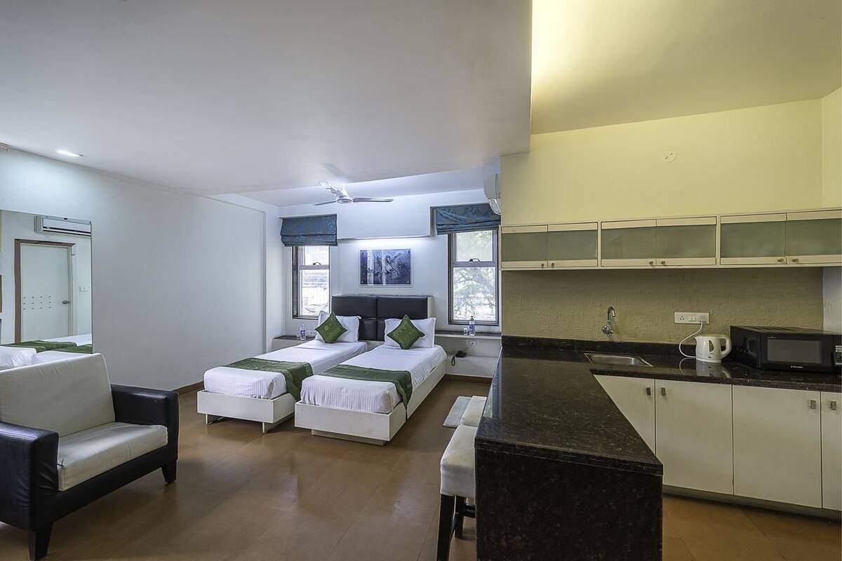 Habitación de hotel con dos camas, un sofá, kitchenette y vistas al exterior.
