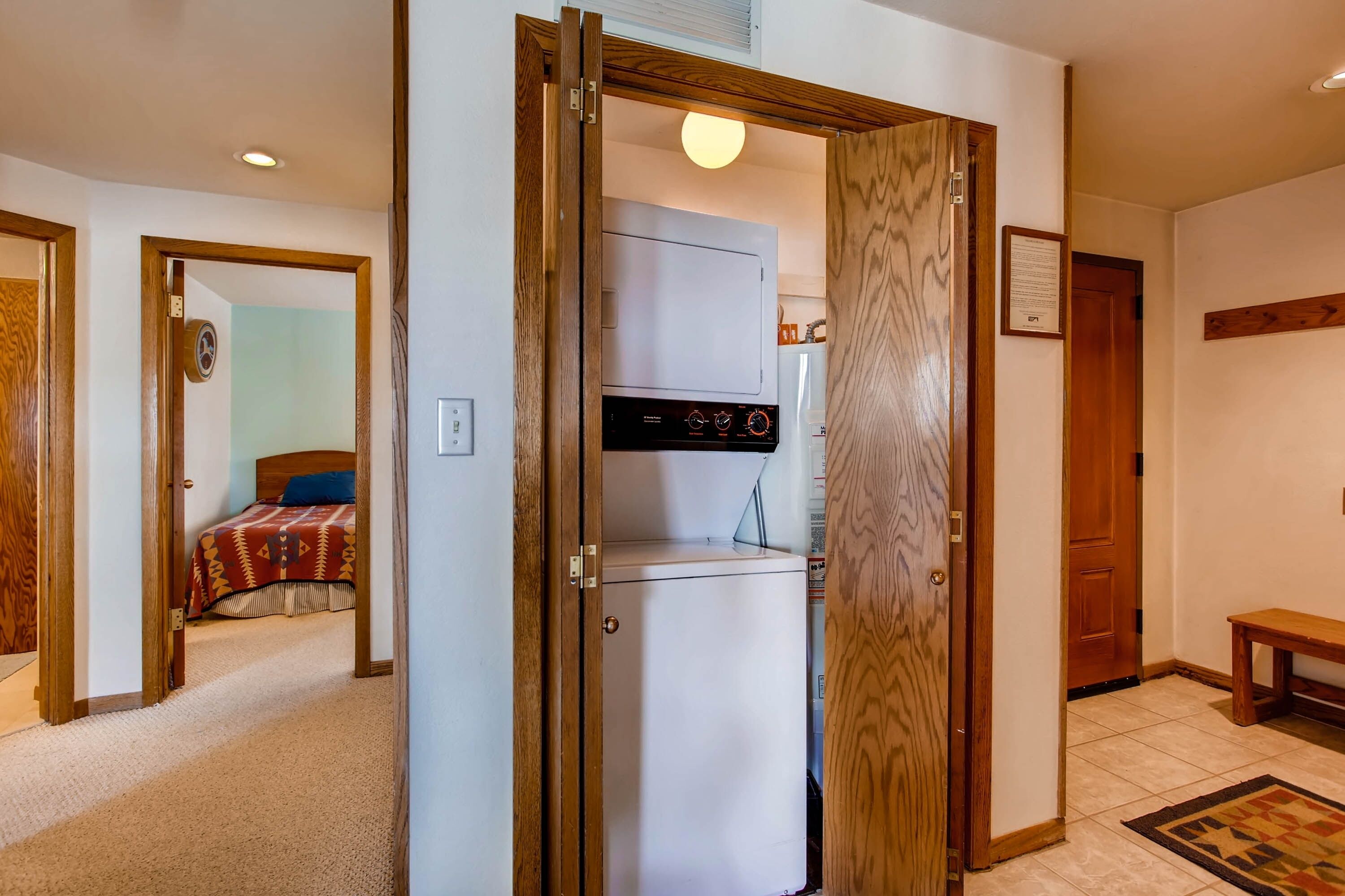 Una habitación con cama, lavadora-secadora incorporada, puerta de madera y un banco.
