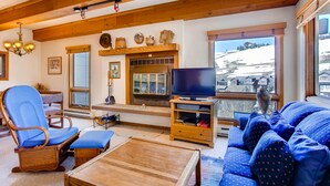 Ein gemütliches Wohnzimmer mit Holzboden, einem Fernseher, einer Couch, einem Sessel und einem Kamin.