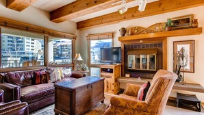 Een gezellige woonkamer met een open haard, houten balken, een televisie en een bank.
