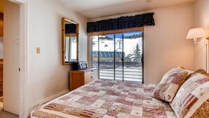 A bedroom with a large bed, a dresser, a mirror, and a window with a view of a ski slope.