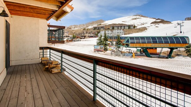 A wooden deck with a metal railing overlooking a snow-covered landscape, including a ski lift and buildings.