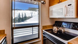 A kitchen with a stove, microwave, and a window overlooking a snowy landscape.
