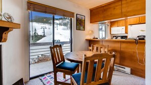 A cozy kitchen with wooden cabinets, a dining table with chairs, and a view of a snowy landscape through a large window.