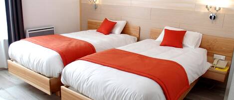Habitación doble con dos camas, cada una con estructura de madera y ropa de cama blanca. Hay dos lámparas fijadas a la pared, una a cada lado de las camas.