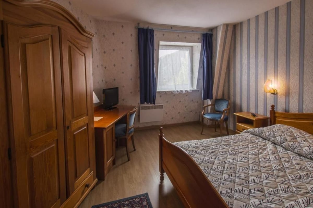 Habitación de hotel con cama, escritorio, silla, armario y ventana con cortinas.