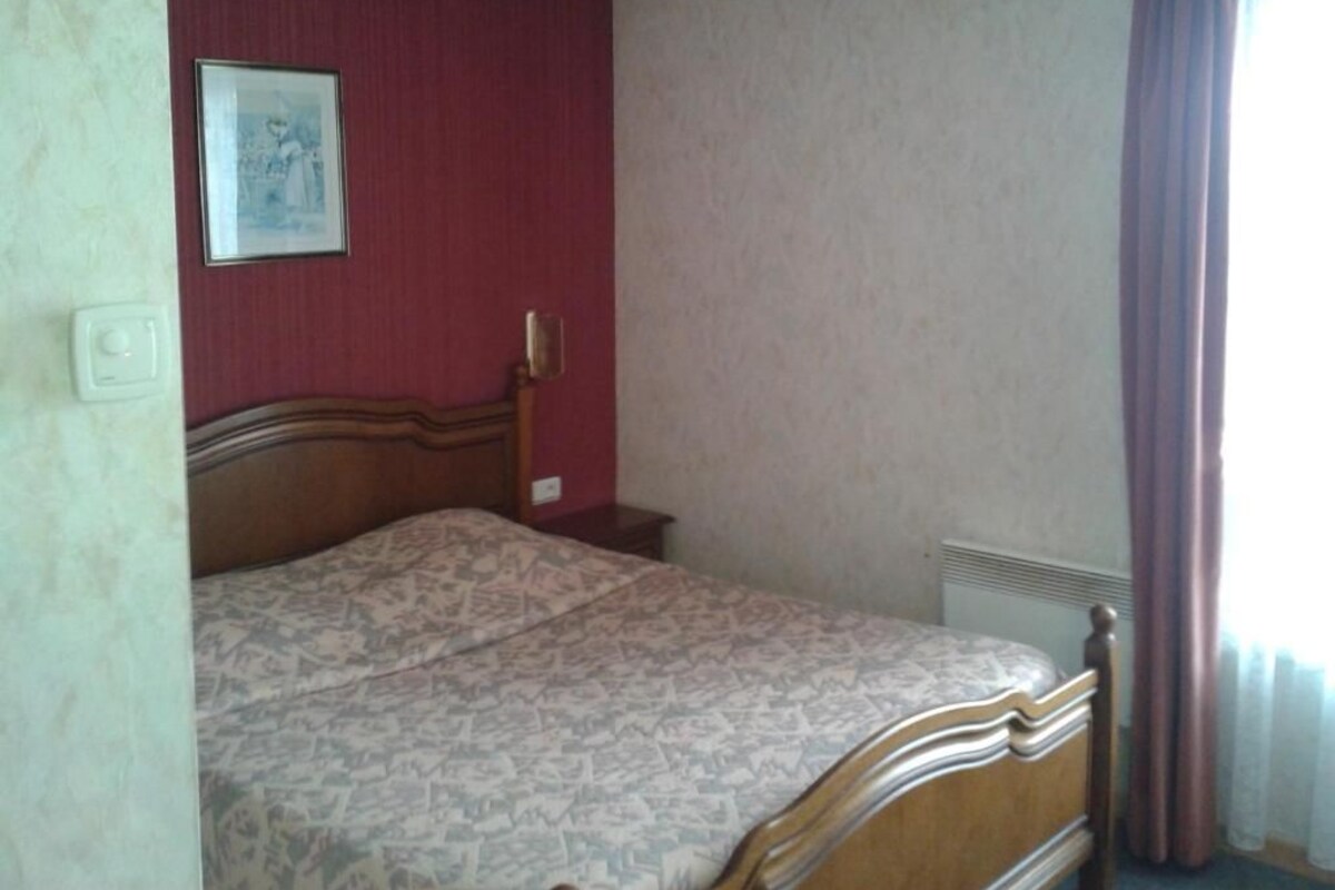 A bedroom with a bed, a nightstand, a wall-mounted light, and a window with curtains.