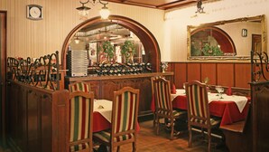 Een restaurantinterieur met houten zithoeken, rode tafelkleden en een wijnrek.