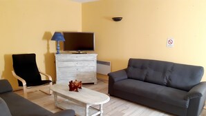 Een woonkamer met een bank, fauteuils, een salontafel, een televisie, een lamp en een dressoir.