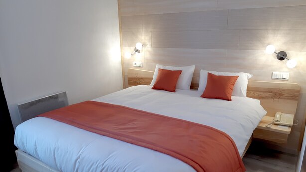 Een hotelkamer met een groot bed, twee nachtkastjes, een nachtkastje met telefoon, en wandlampen.