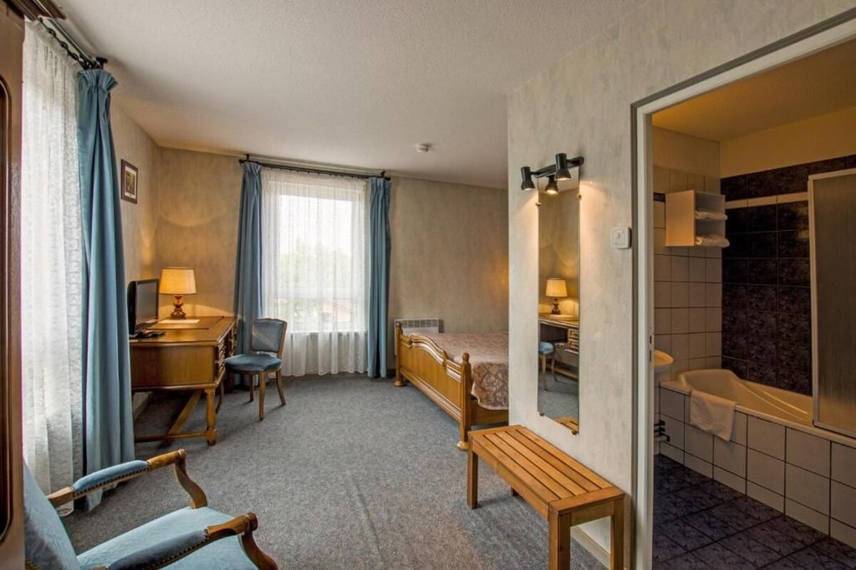 A hotel room with a desk, chair, bed, bedside table, and a bathroom with a bathtub and shower.