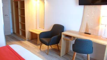 Une chambre moderne comprenant un lit, un bureau, deux chaises, une armoire, un miroir et un téléviseur.