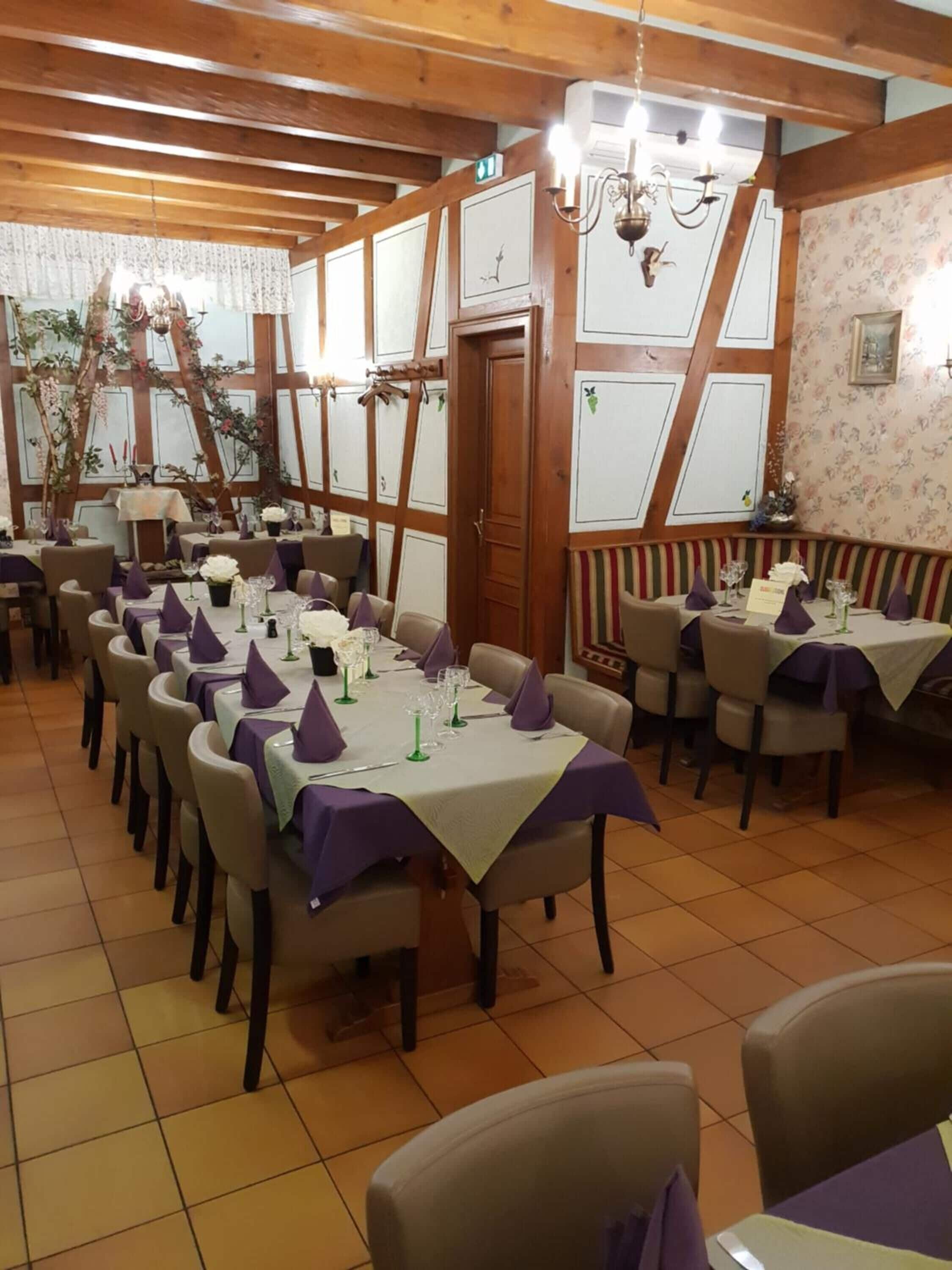 A restaurant with wooden beams, tiled floors, and tables set with purple napkins and glassware.