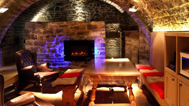 Una habitación de paredes de piedra con chimenea, asientos de cuero y una mesa de madera.