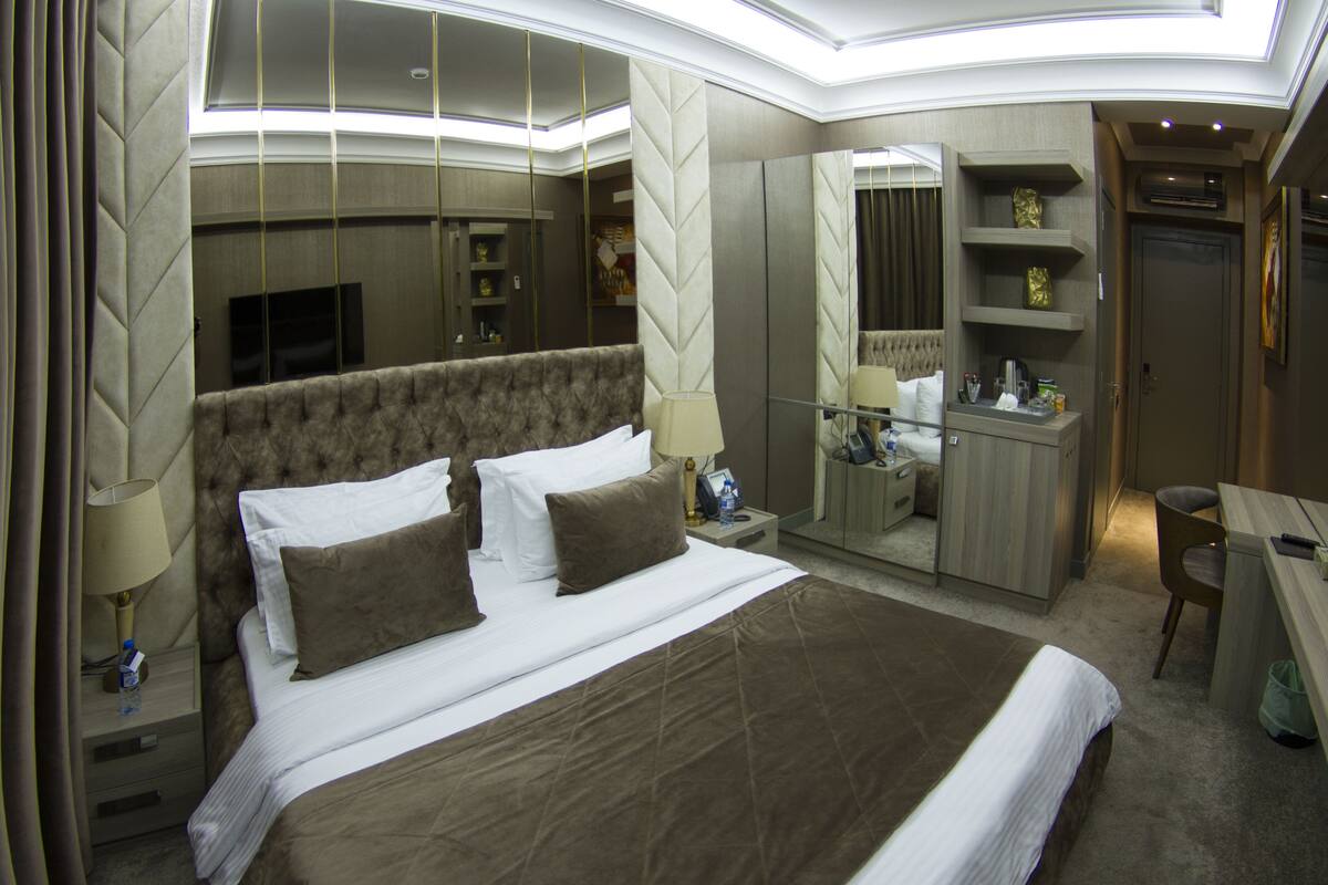 A hotel room with a large bed, a desk, a chair, a mirror, and a wardrobe.