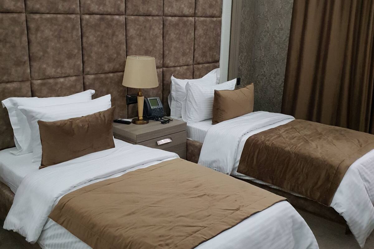 A hotel room with two beds, each with white and brown bedding, a nightstand with a lamp and phone, and a large padded headboard.