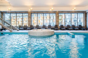 Ein Pool mit Liegestühlen und Whirlpool, umgeben von großen Fenstern mit Blick auf ein Gebäude.
