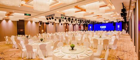 A banquet hall with round tables, white chairs, and chandeliers.